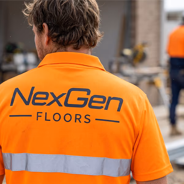 Worker wearing an orange shirt with NexGen Floors logo on the back at a work site.