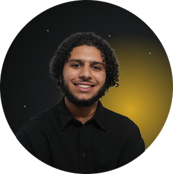 Portrait d'un homme souriant aux cheveux bouclés et barbe, portant une chemise noire.