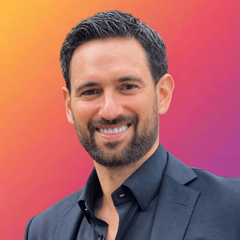 Smiling man with short dark hair and beard wearing plaid suit jacket and checkered shirt.