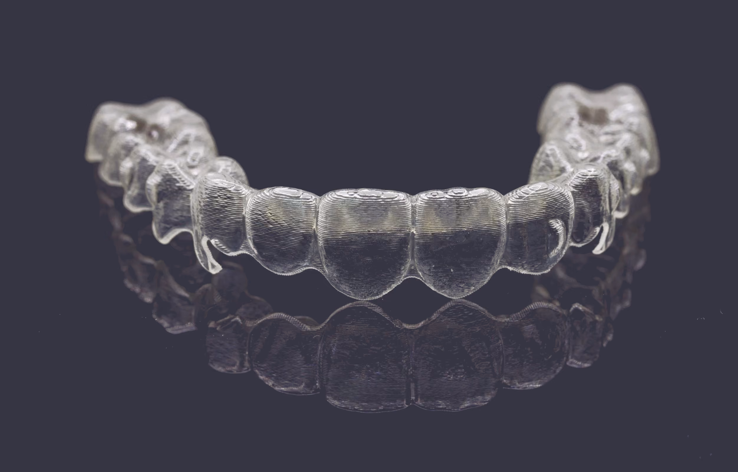 Set of clear aligner trays shown against a dark background.