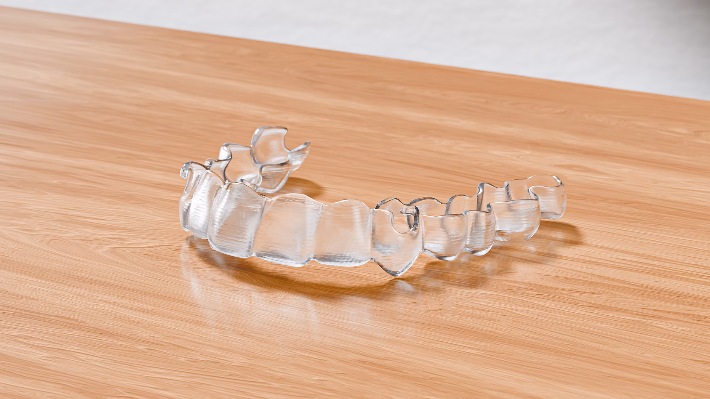 A single clear dental retainer resting on a polished wooden surface, showing the mold of teeth.