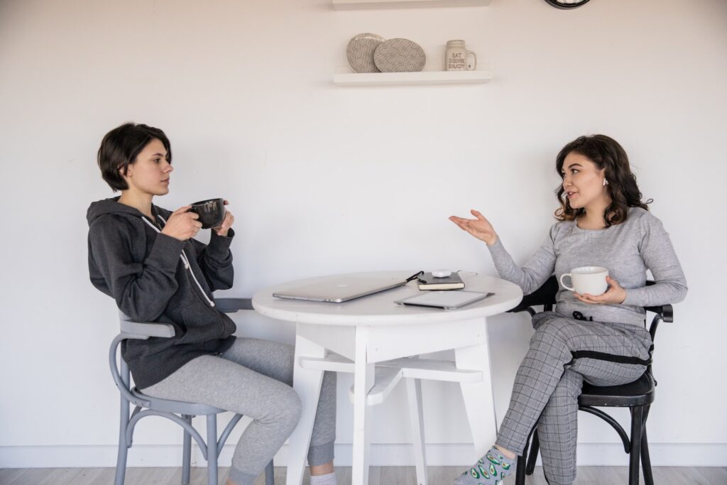 Zwei Frauen sitzen an einem Tisch, führen ein Gespräch und trinken Tee.