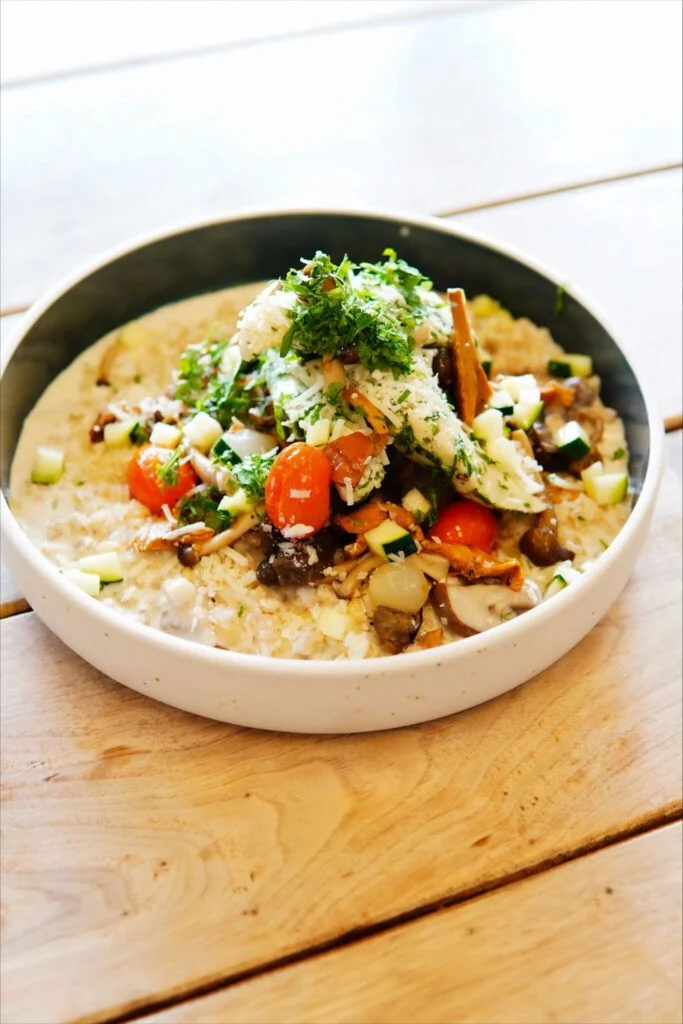 Close-up of a spoon lifting foam-covered gourmet dish with broth and garnishes in a bowl.