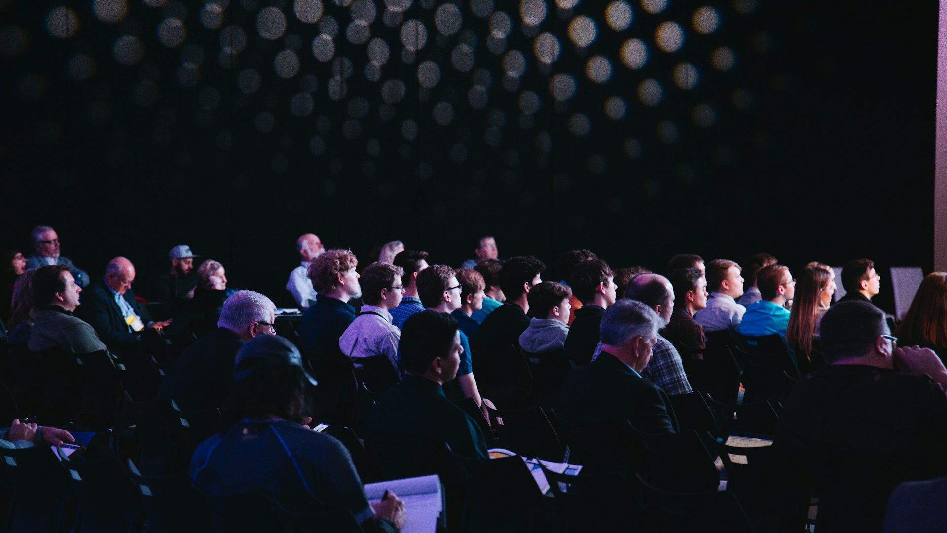Publiek luistert naar een spreker in een verduisterde conferentiezaal