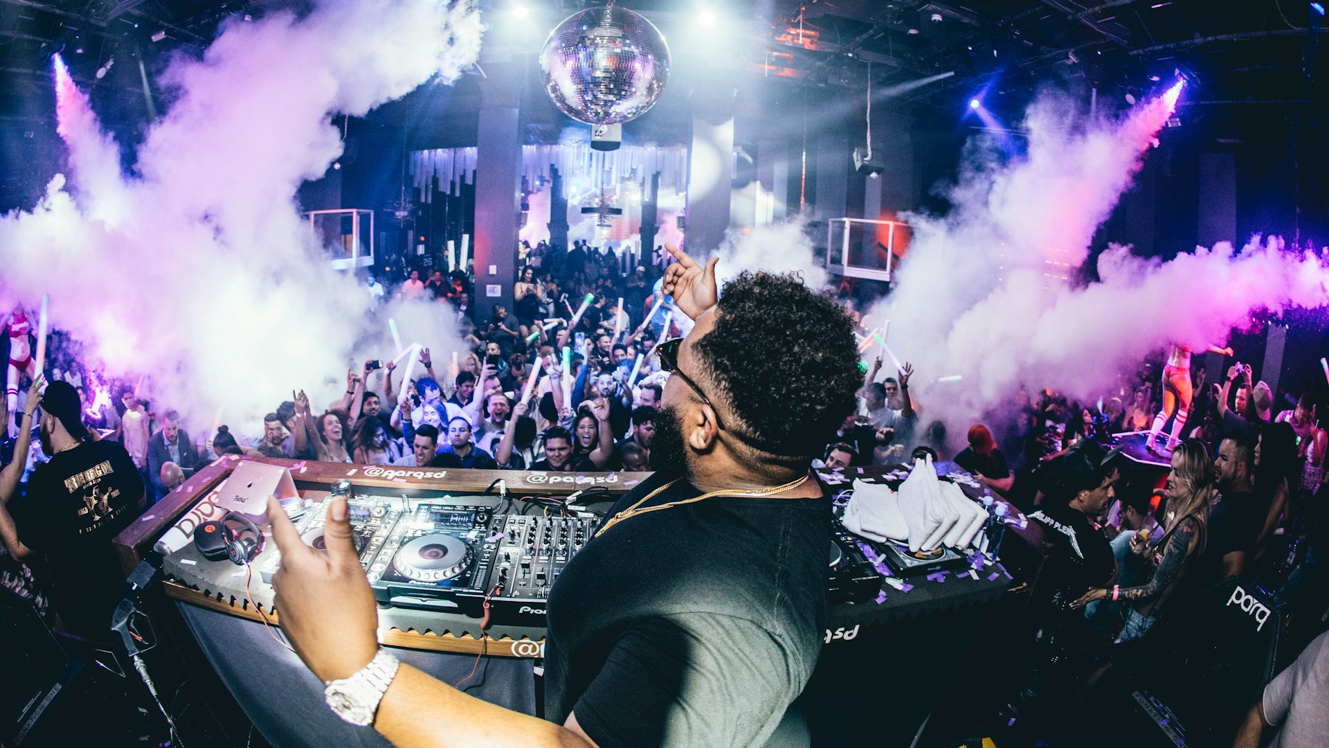 DJ op een podium met paarse rookeffecten en een lichtshow boven het publiek