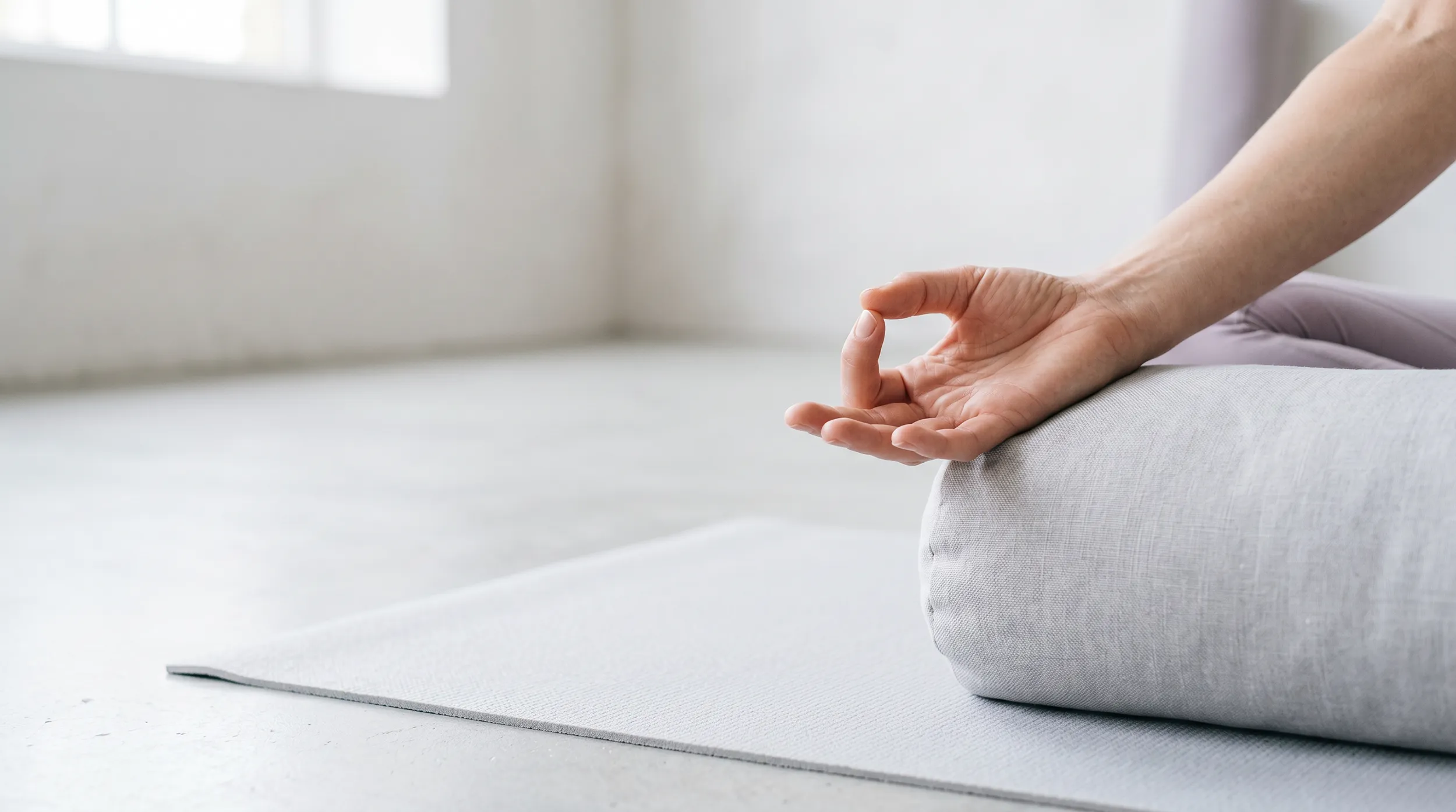 Close-up of a person’s hand in a meditation mudra pose resting on a cushion on a yoga mat.