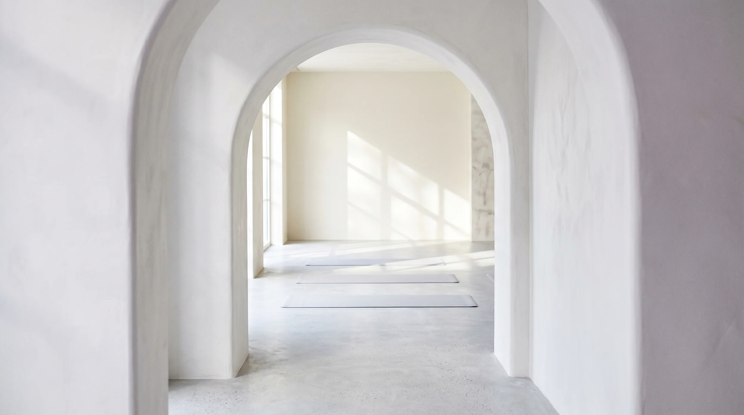 Minimalist bright yoga room with arched doorway and three mats on polished concrete floor.