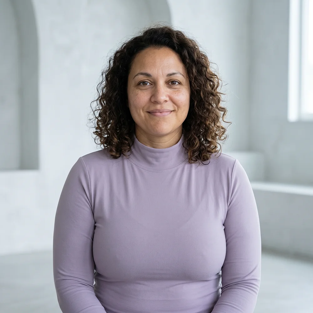 Smiling woman with curly hair wearing a lavender turtleneck in a bright room.
