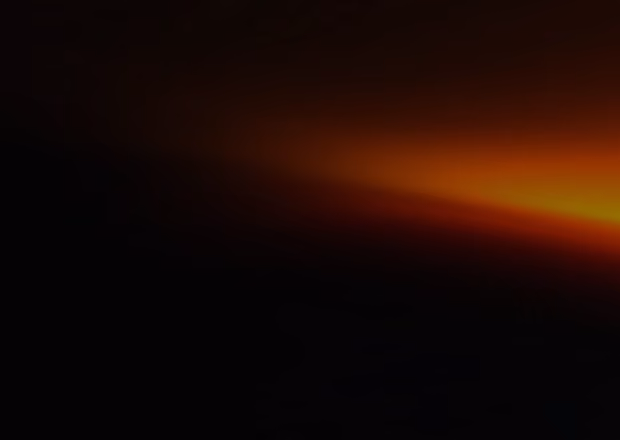 Faint orange light fading into darkness, appearing like a distant sunset or glow on the horizon in a dark environment.