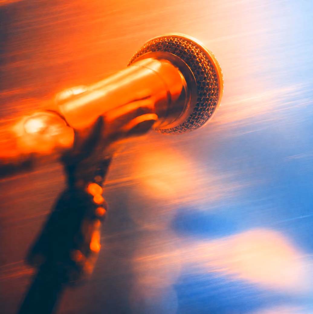 Close-up of a microphone head with warm orange and cool blue lighting creating a blurred gradient background.