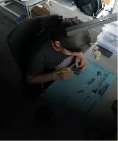 Person sitting at a desk working on a project with tools and electronics components on a blue mat, using a gesture-controlled headset.