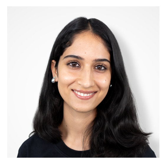 Portrait of a smiling woman with long dark hair wearing pearl earrings and a black top against a white background.