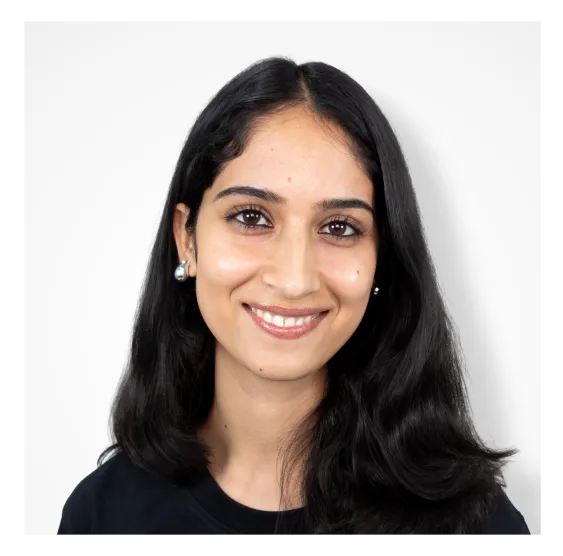 Portrait of a smiling woman with long dark hair wearing pearl earrings and a black top against a white background.