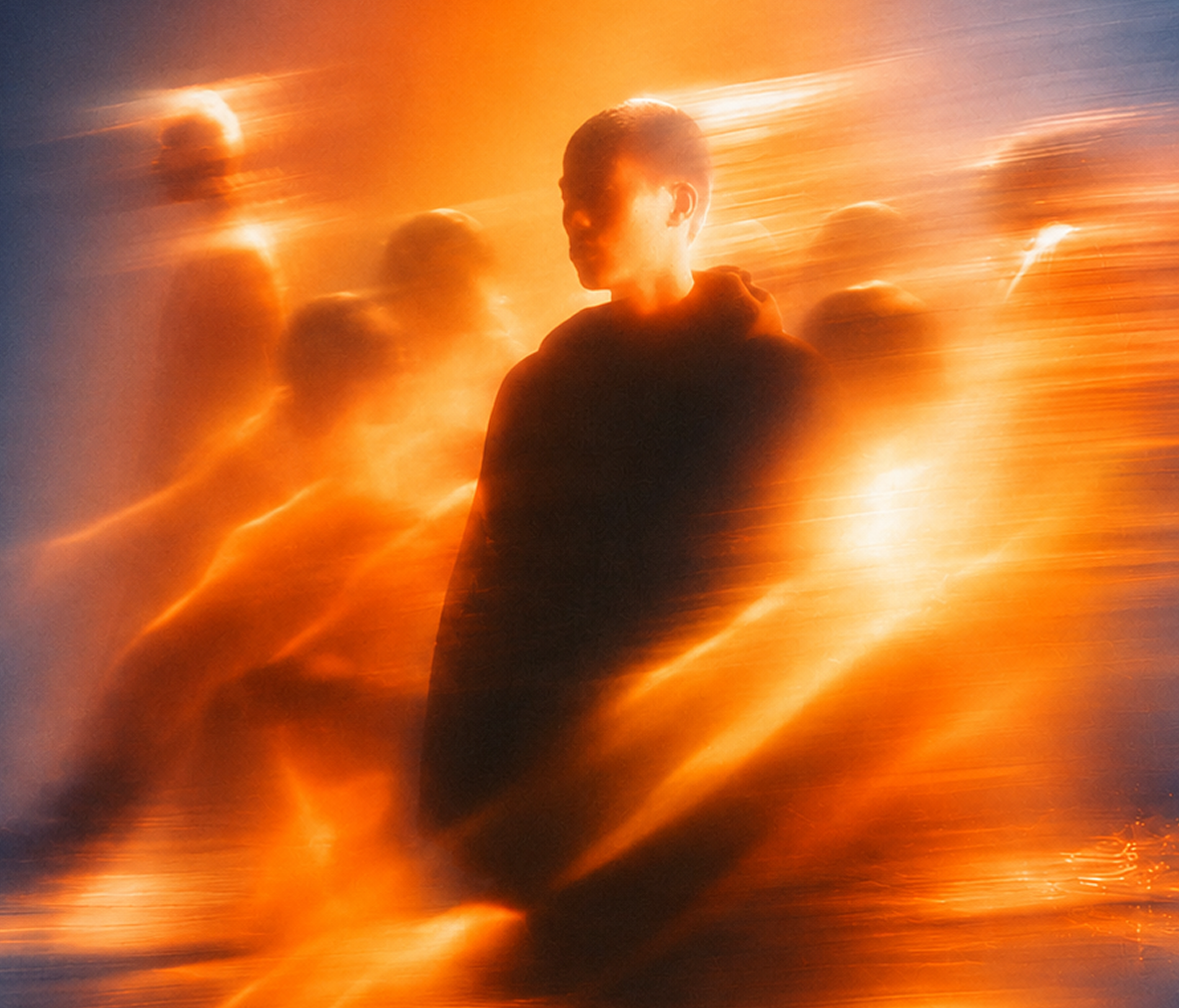 Silhouette of a person in a dark hoodie surrounded by streaks of orange and yellow light with blurred, ghost-like figures in the background, creating a dynamic, abstract effect.