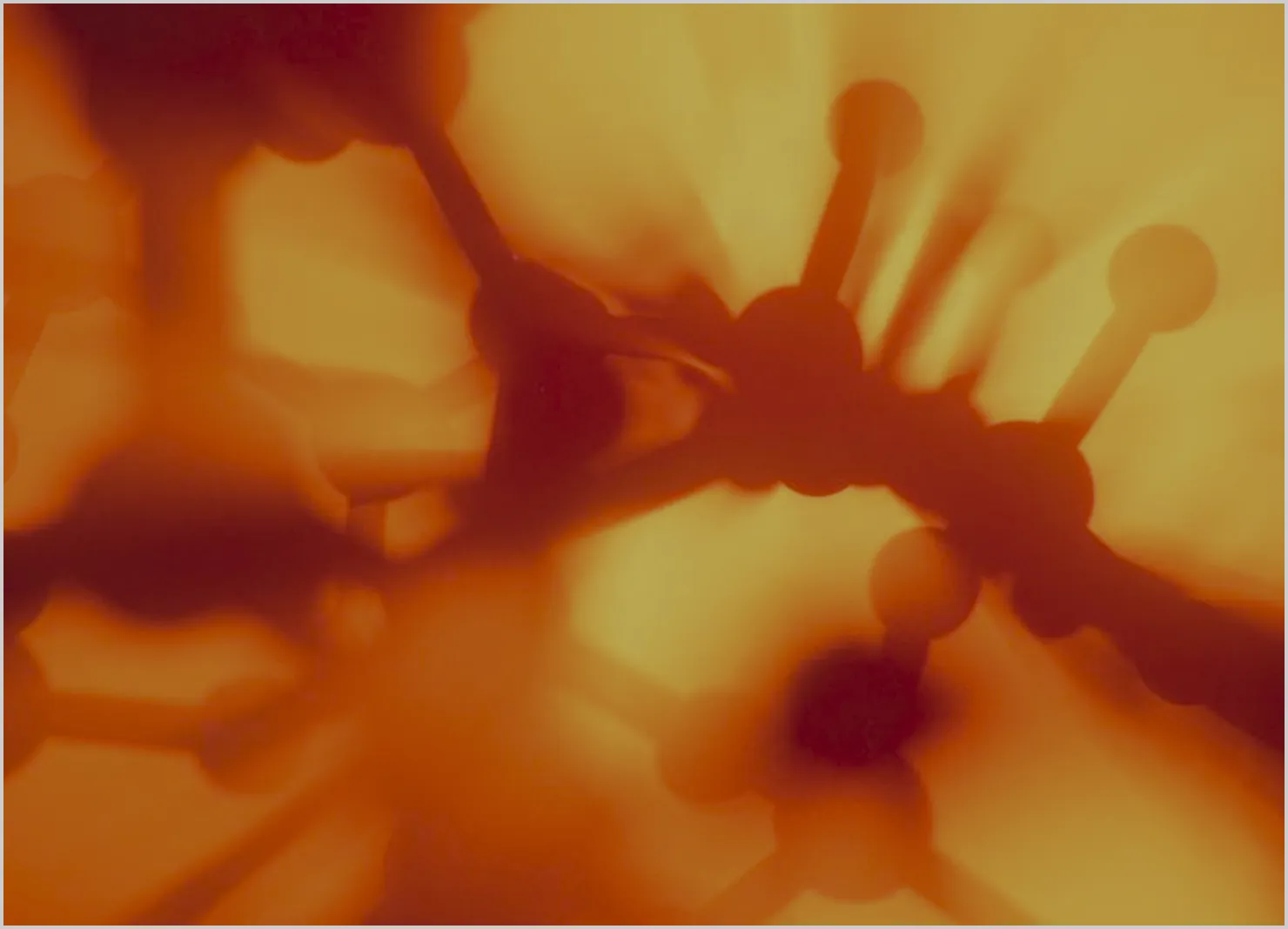 Abstract close-up of interconnected molecular structure with spherical nodes and cylindrical bonds in warm orange and yellow tones.