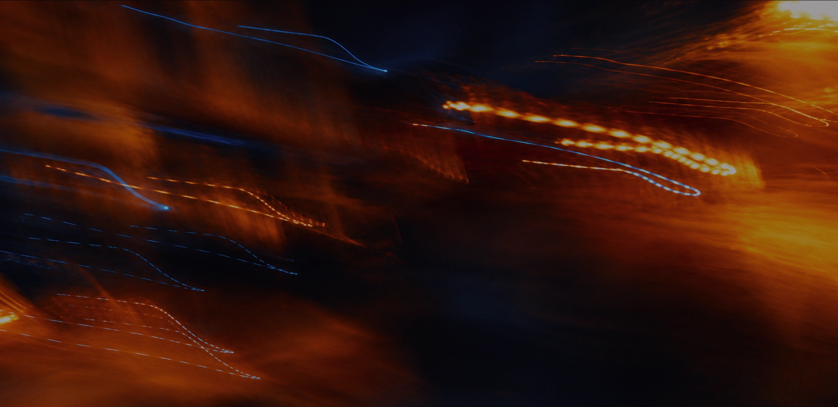 Abstract image with blurred orange and blue light streaks on a dark background.
