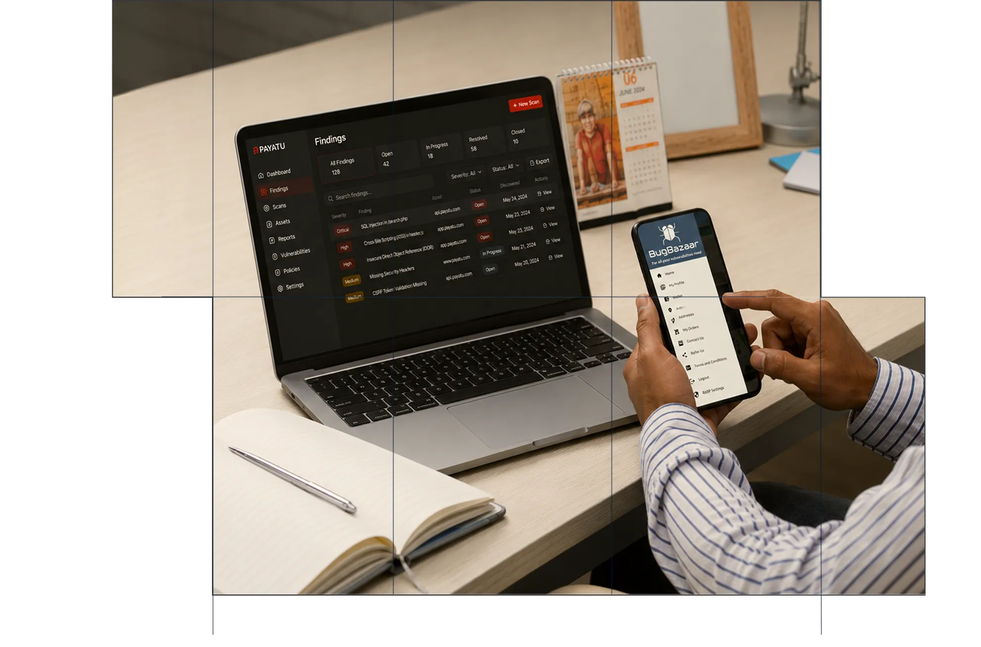 Person holding a smartphone displaying Bugbazaar app menu while sitting at a desk with an open laptop showing a Payatu security findings dashboard. The desk also has a spiral calendar, an open notebook with a pen, and a lamp.
