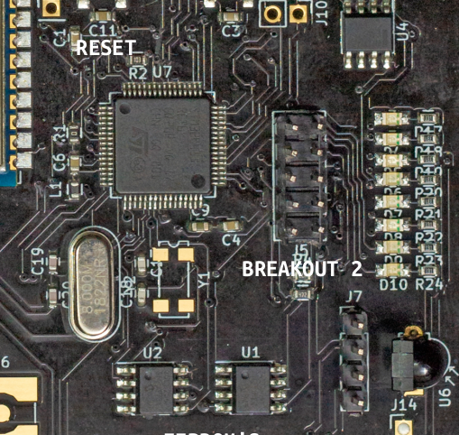 Close-up view of a computer circuit board with various electronic components including chips, connectors, capacitors, and resistors. Labels 'RESET' and 'BREAKOUT 2' are visible on the board near specific components.