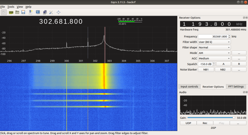 Gqrx software-defined radio interface displaying a frequency spectrum centered at approximately 302.6818 kHz with signal peaks and a waterfall visualization below showing horizontal signal bands. The right panel shows receiver options including hardware frequency at 301.488000 MHz, user-set filter width of 80 kHz, AM mode selected, medium AGC, and squelch set to -150 dB. Audio control gain is set to 50 dB with UDP option active.