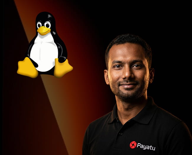 Man with short black hair and a beard wearing a black collared shirt with a red and white Payatu logo, standing against a dark background with a gradient brown-orange diagonal light beam and a large Linux Tux penguin logo on the left.