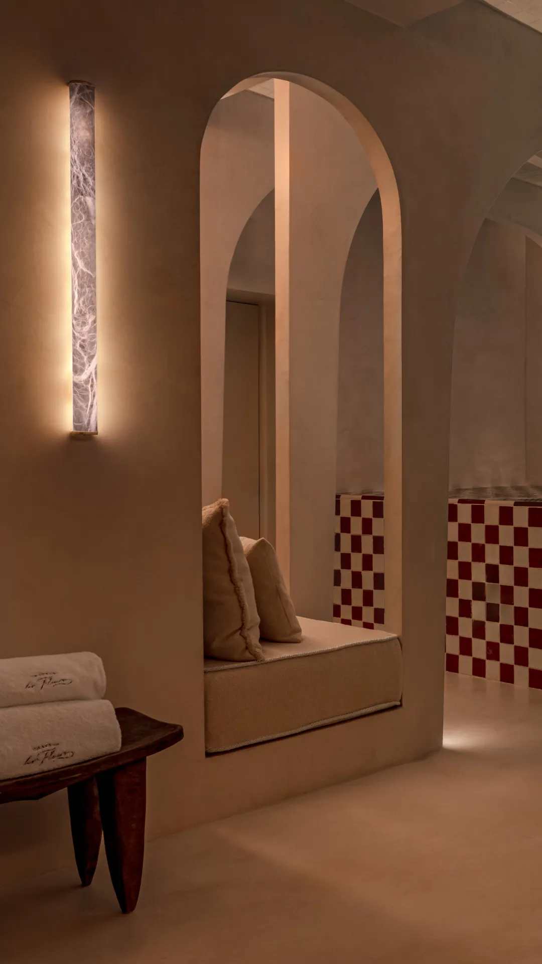 Espace spa avec coussins sur banquette, lumière chaude murale et mur à carreaux rouges et blancs.
