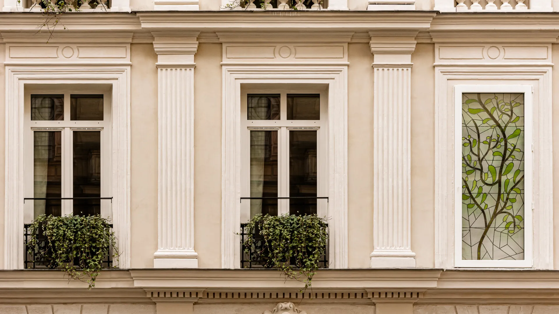 Beige facade with two windows and a glass door decorated with stylized green foliage.