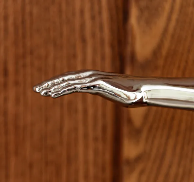 Poignée de porte chromée en forme de main sculptée posée devant un fond en bois.