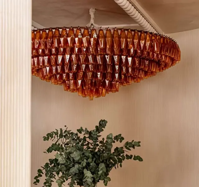 Plafonnier en verre ambré suspendu avec plante verte en contrebas dans une pièce beige.