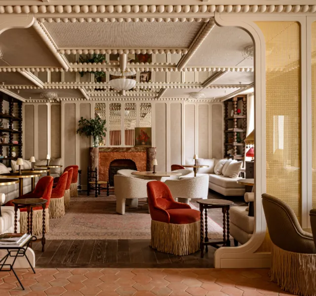 Salon élégant avec fauteuils rouges à franges, canapés beiges et cheminée en pierre rouge.