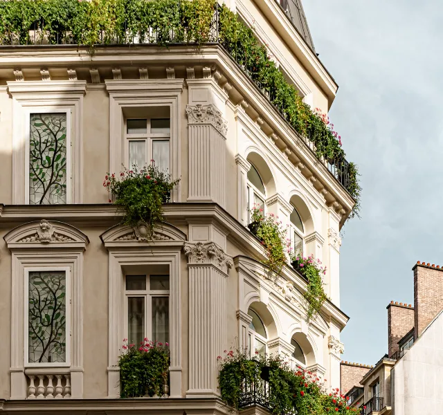 Façade d'un immeuble classique avec balcons fleuris et fenêtres, ciel clair en arrière-plan.