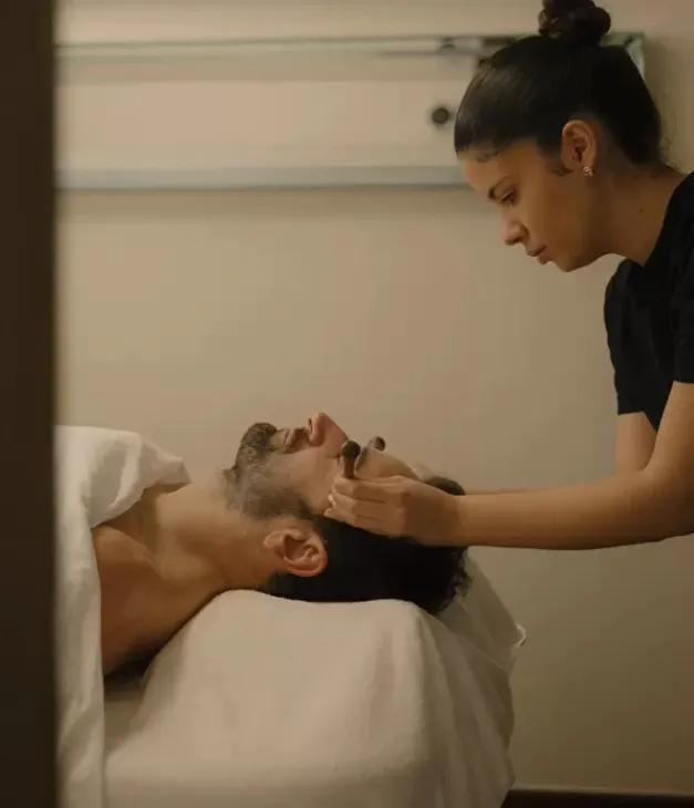 Une femme effectue un soin du visage sur un homme allongé sur une table de massage.
