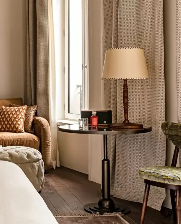 Salon avec canapé brun, ottomane, table ronde avec lampe et chaise vintage près de la fenêtre.