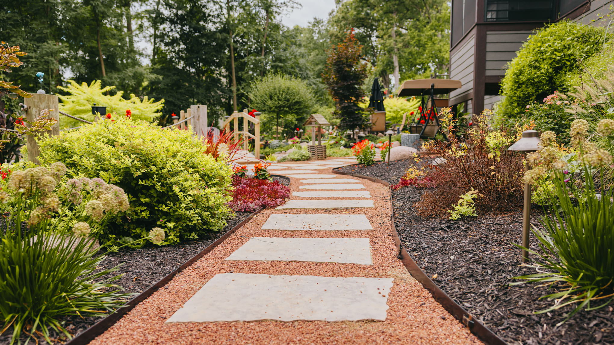 Stone paver walkway winding through layered planting beds lit by low garden lights.