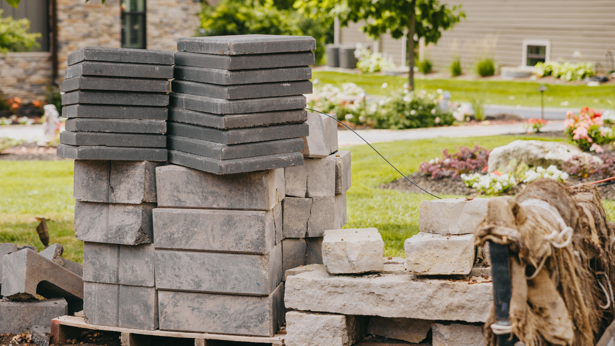 Pallets of grey pavers and wall block staged on a lawn at the start of a hardscape build.