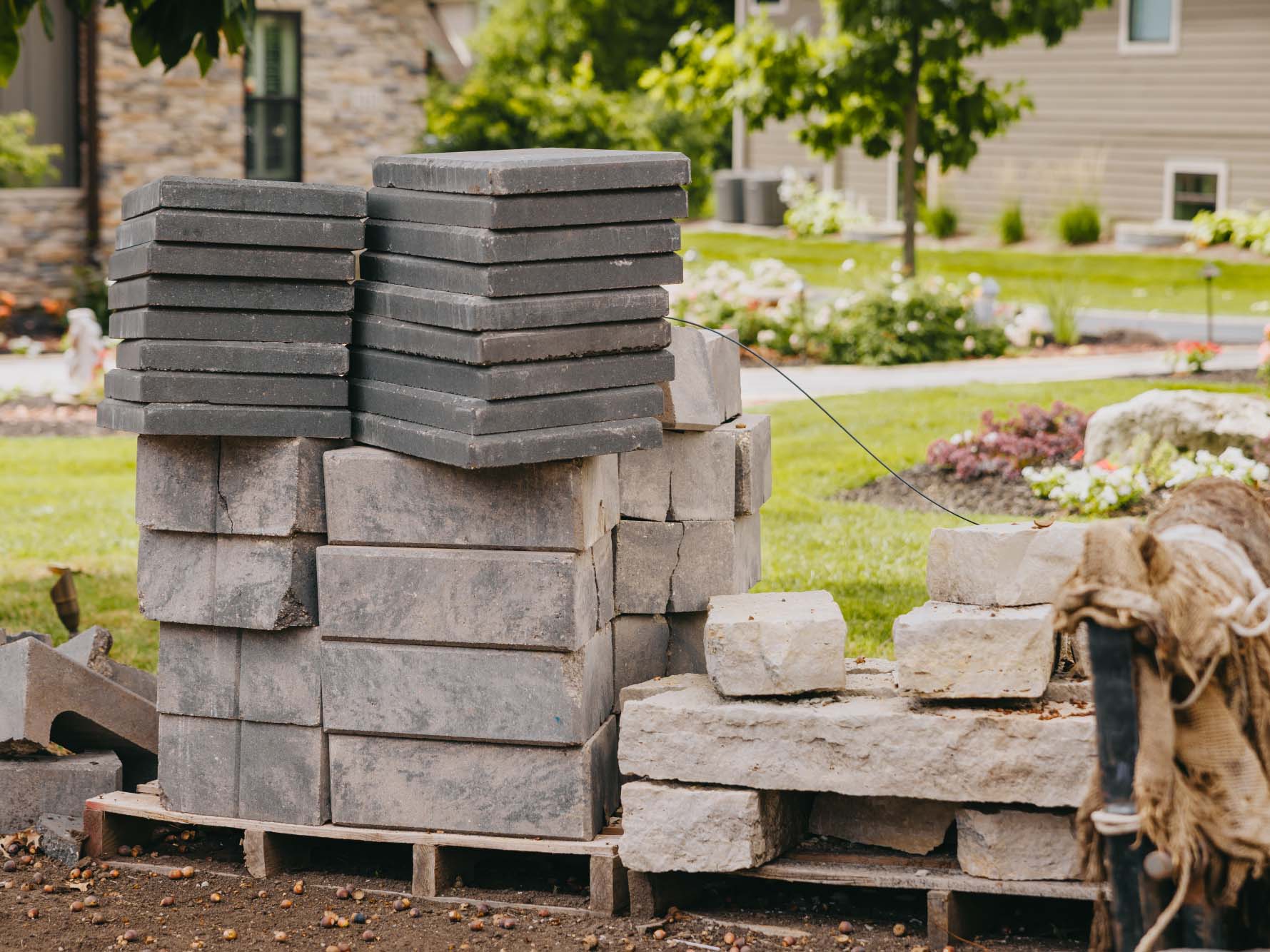 Stacked grey pavers and natural stone on a pallet at a landscaping worksite.