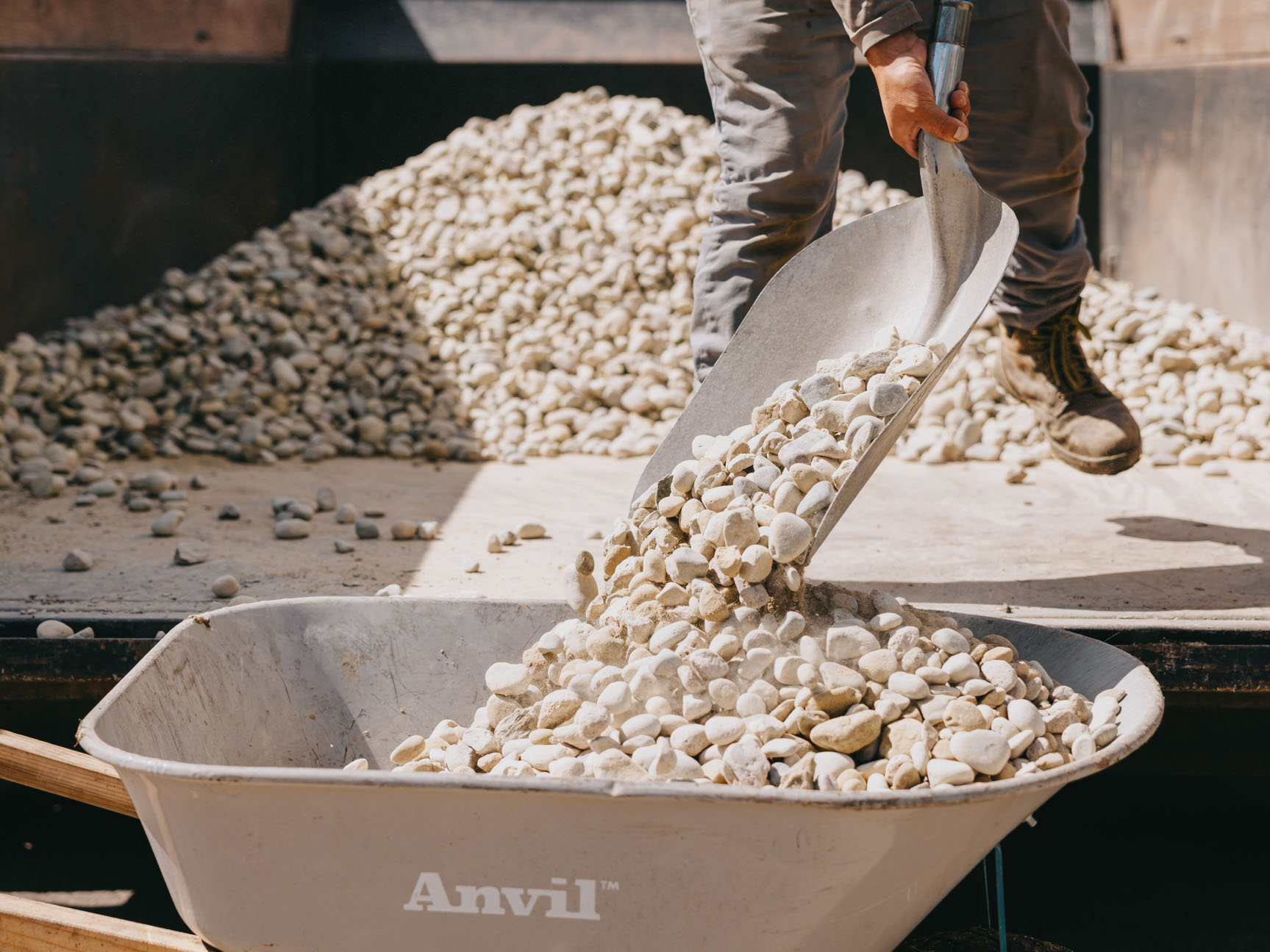 Crew member loading a wheelbarrow with river rock during a hardscape installation.