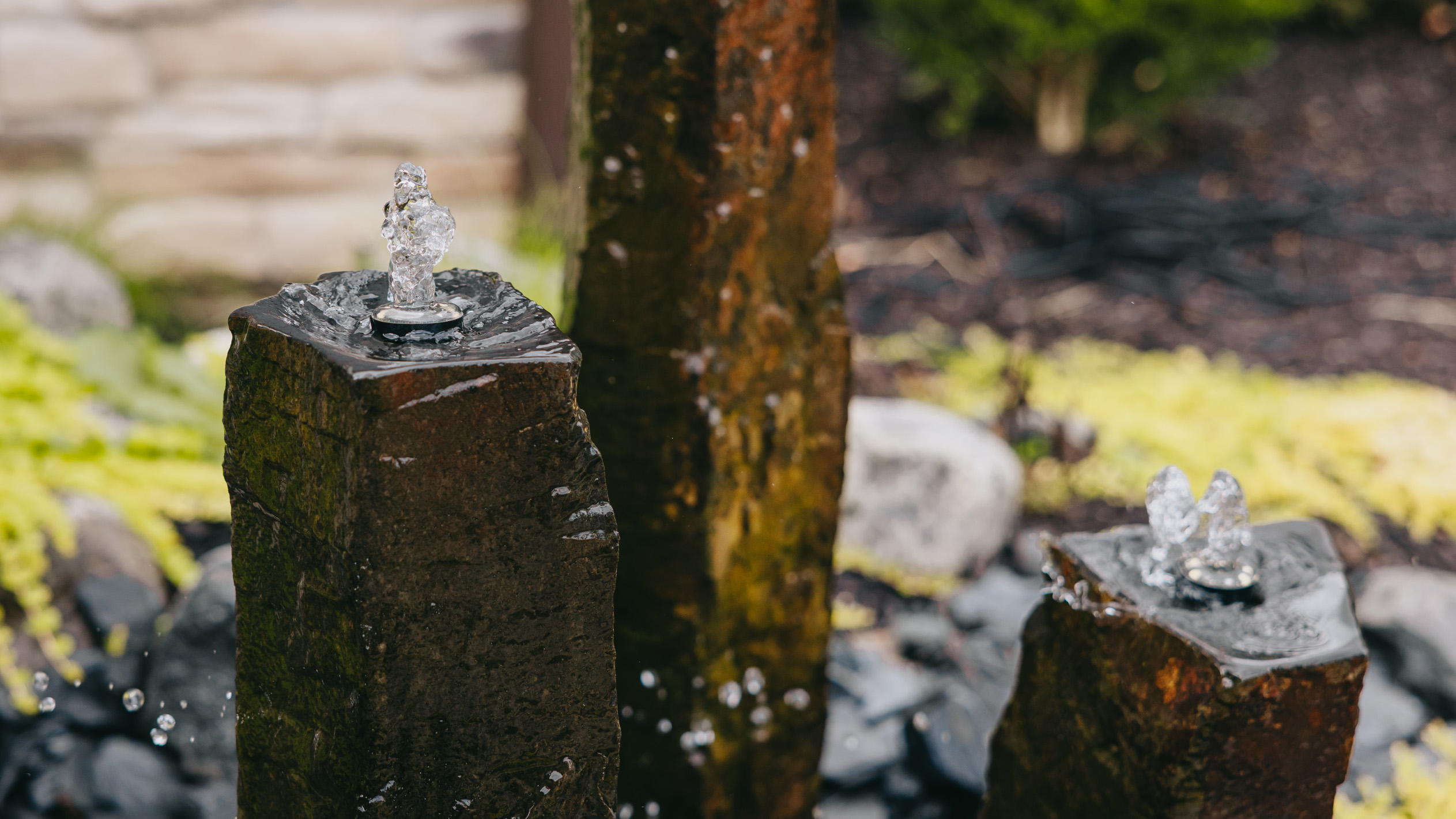 Three bubbling stone fountains set into a boulder and perennial garden.