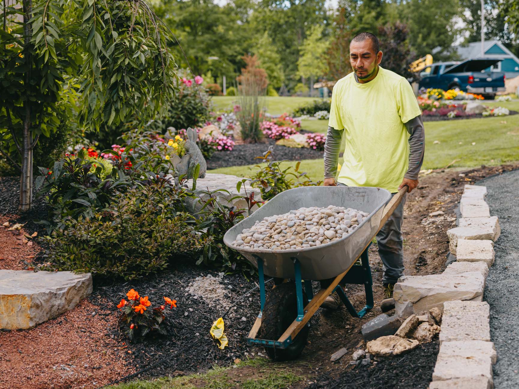 Crew member pushing a wheelbarrow of decorative stone across a garden under installation.