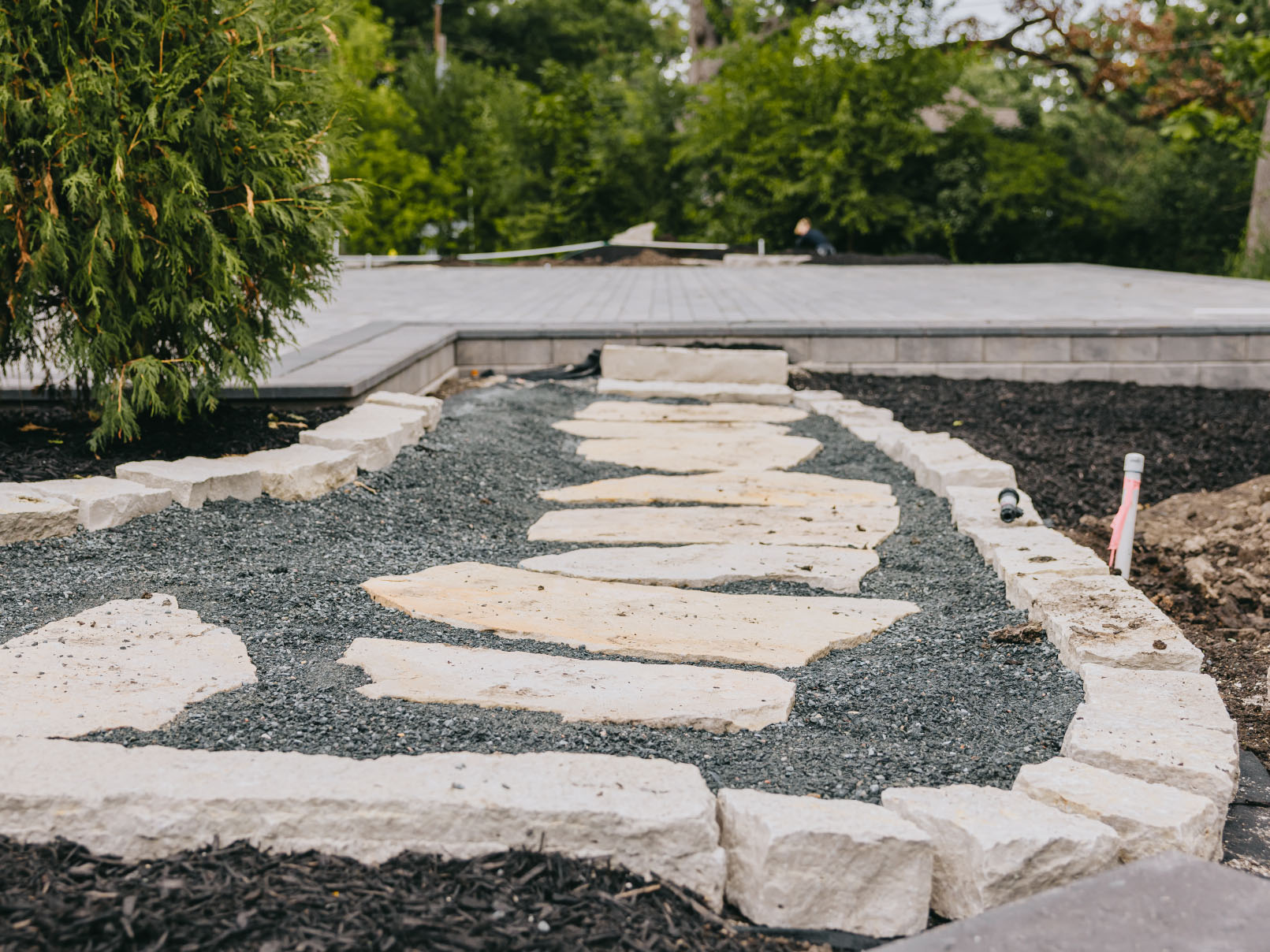Stone walkway under construction across a levelled base in a back garden.