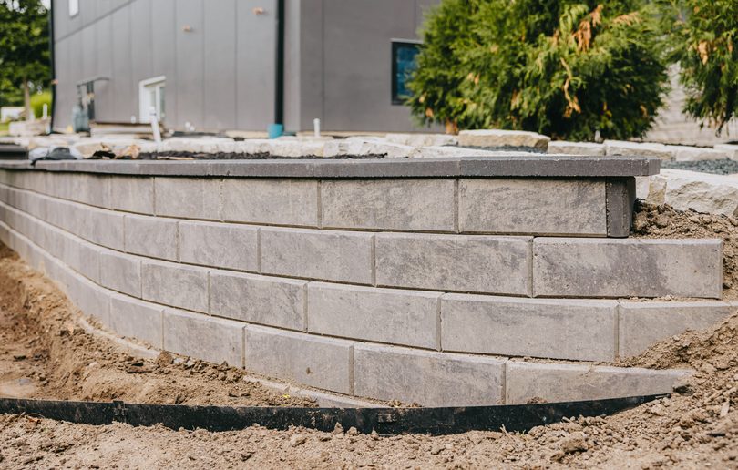 Concrete block retaining wall installation in progress beside a modern home.
