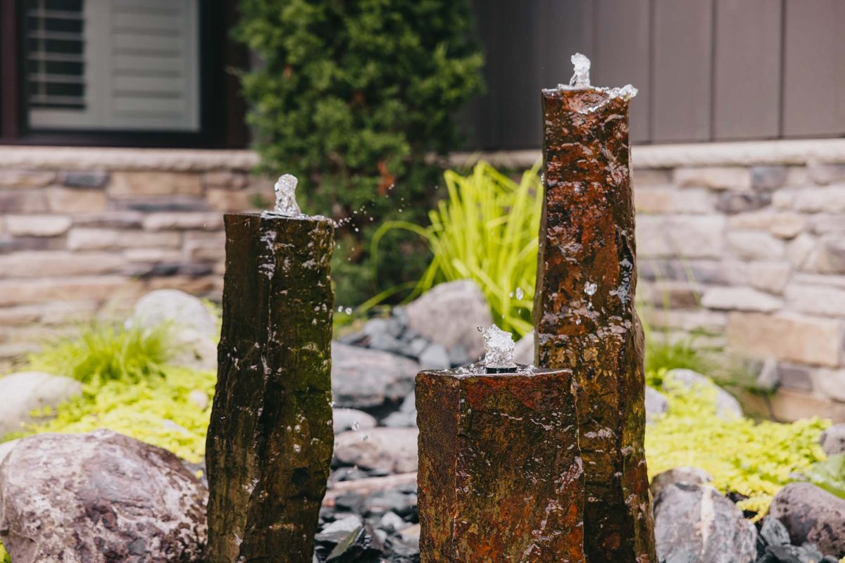 Three vertical stone fountains bubbling in a boulder-edged front garden.