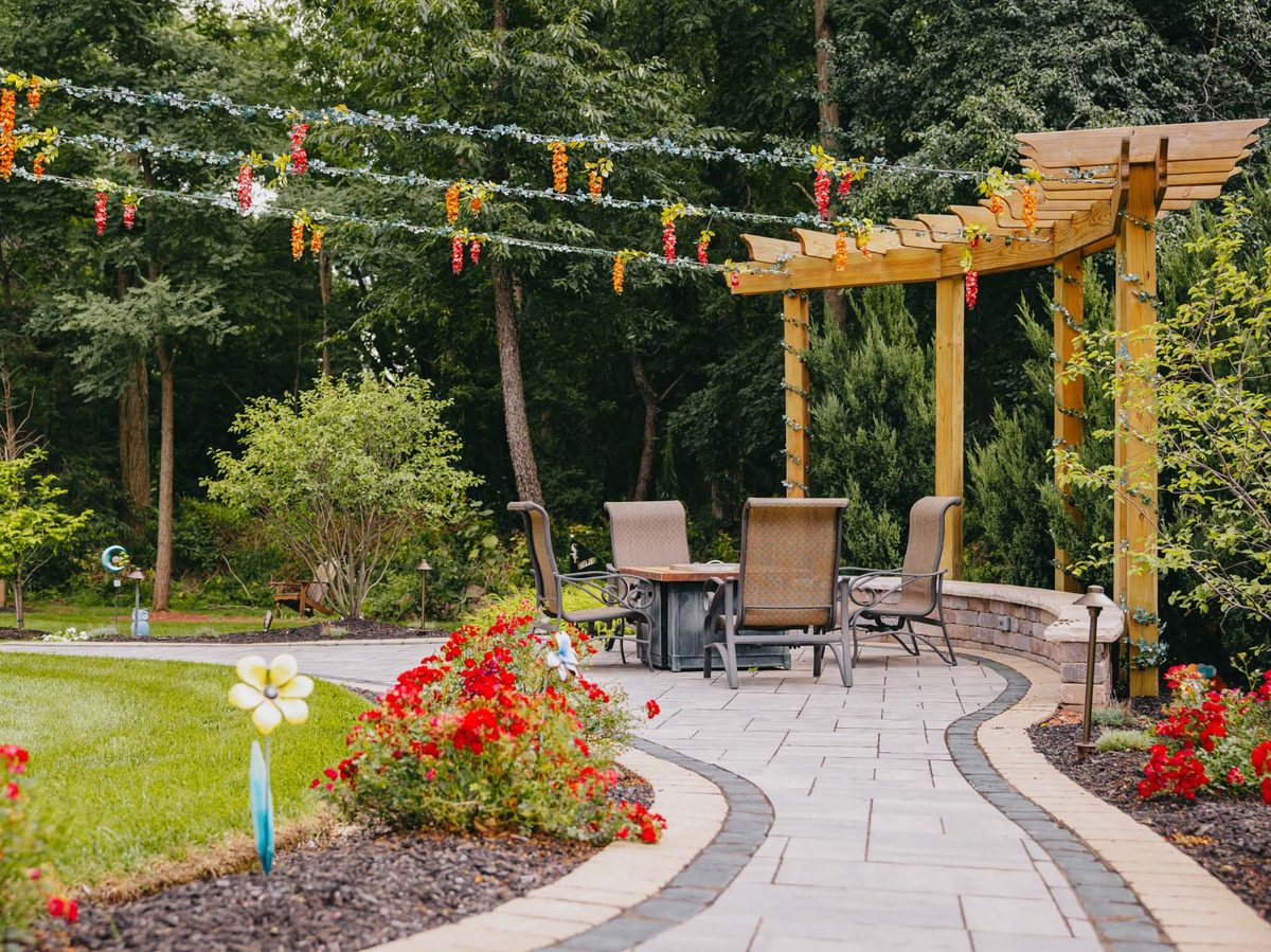 Timber pergola over a paver patio framed by red annuals and mature shrubs.