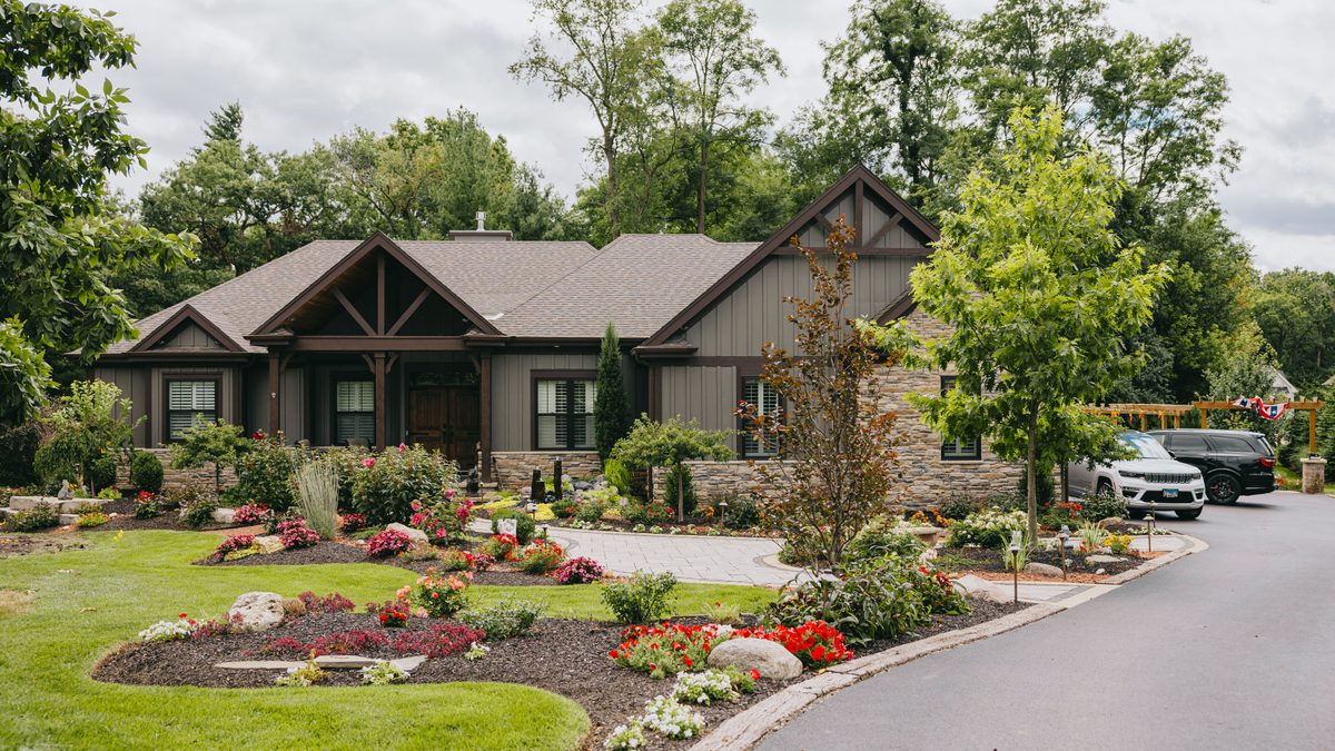 Craftsman-style home with layered front planting beds, flowering perennials and a curved lawn edge.
