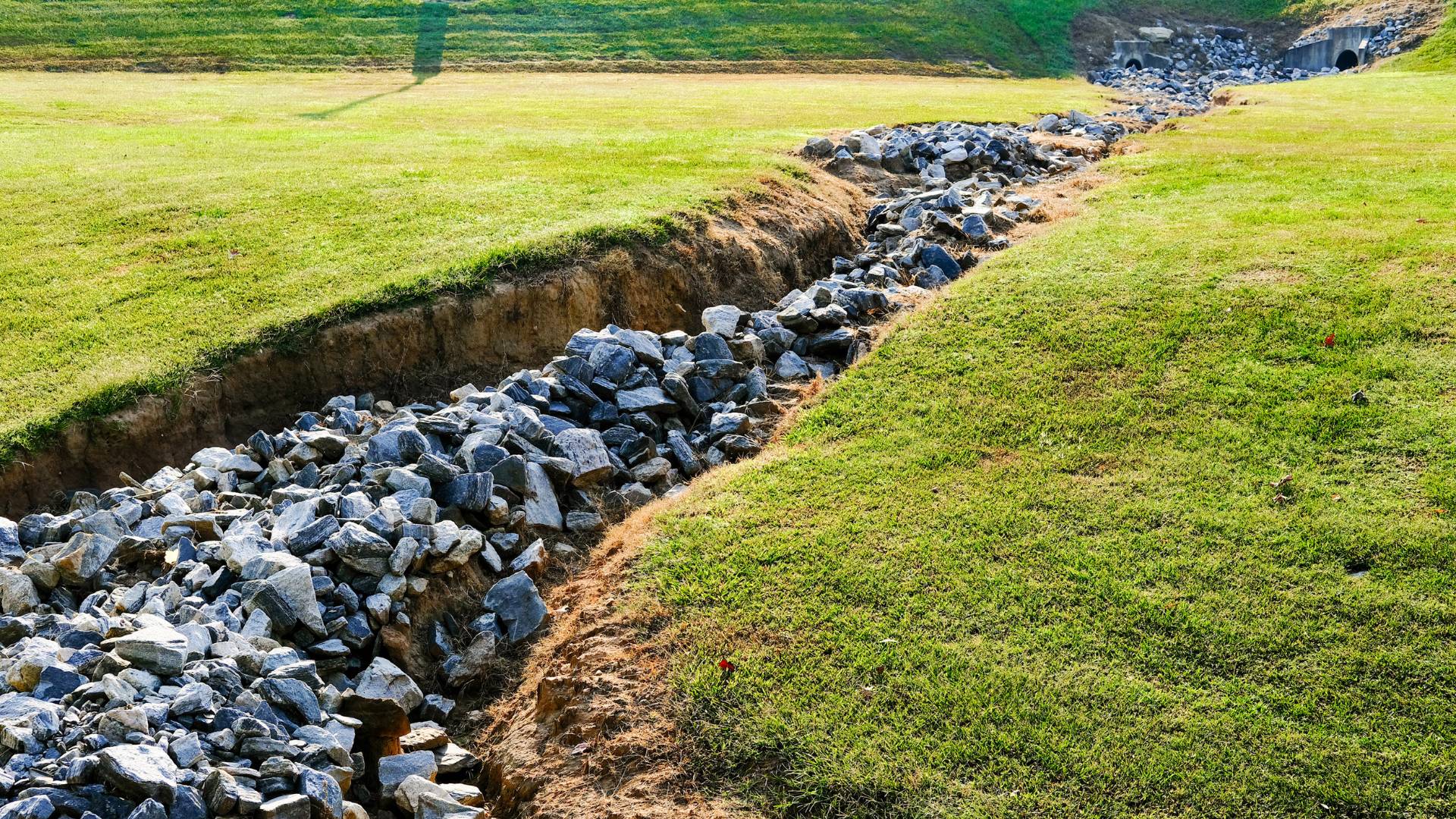 Dry creek bed lined with large rocks running through green grassy terrain.