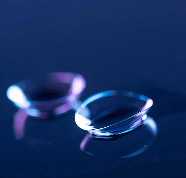 Two transparent contact lenses placed on a dark reflective surface with blue and purple lighting.