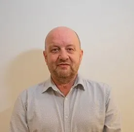 Portrait of a bald middle-aged man with a beard wearing a light gray buttoned shirt.