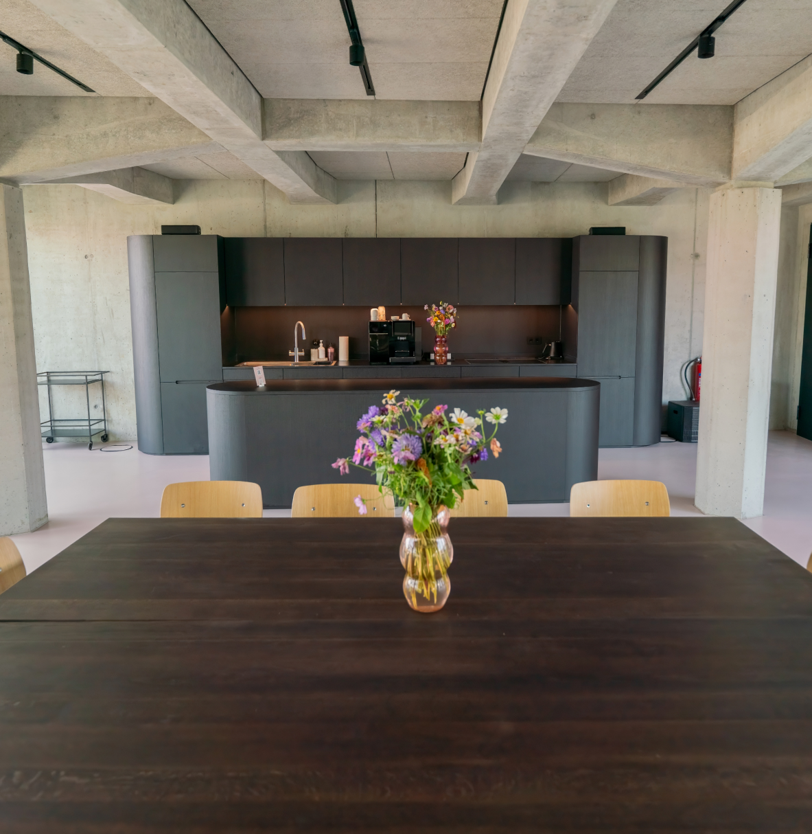 Moderne Küche mit dunklen Schränken, Kochinsel und einem großen Holztisch davor mit einem Blumenstrauß in einer Vase.