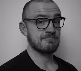 Black and white portrait of a man with glasses, short hair, a mustache, and a beard.