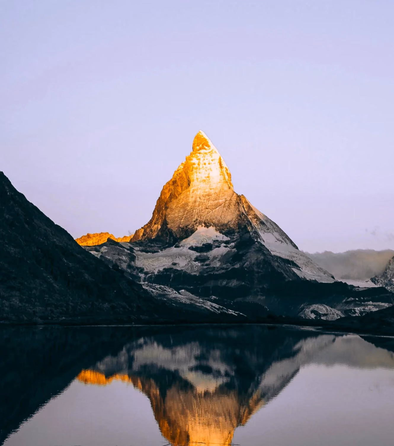 Mountain peak lit by sunrise, mirrored in a still lake