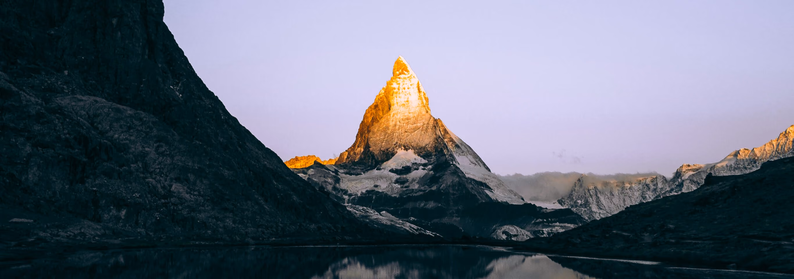 Mountain peak lit by sunrise, mirrored in a still lake